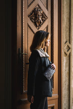 Kép betöltése a galériamegjelenítőbe: Borsetă elegantă din piele neagră cu model modern, purtată crossbody de o femeie, vedere frontală, fermoar și curea reglabilă