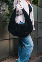 Load image into Gallery viewer, Persoană care poartă o geantă neagră pe un umăr, cu fundal neclar.

