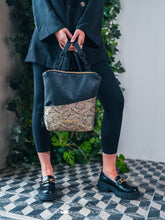 Kép betöltése a galériamegjelenítőbe: Persoană care ține o geantă neagră elegantă cu buzunar decorativ, purtând ținută neagră.
